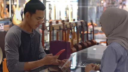 An upwardly mobile Asian Muslim man using a mobile phone - smartwatch to pay for a product at a sale terminal with nfc identification payment for verification and authentication