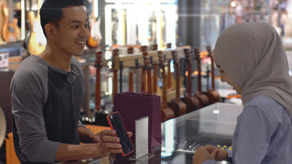 Fototapeta na wymiar An upwardly mobile Asian Muslim man using a mobile phone - smartwatch to pay for a product at a sale terminal with nfc identification payment for verification and authentication
