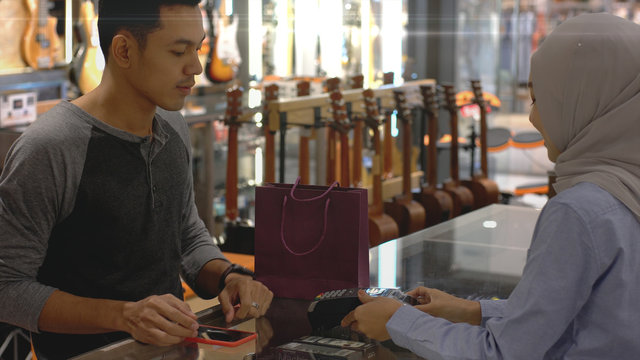 An upwardly mobile Asian Muslim man using a mobile phone - smartwatch to pay for a product at a sale terminal with nfc identification payment for verification and authentication