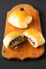 Home-baked Beef Russian Bierocks on a rustic wooden board on a black surface, side view. Close-up.