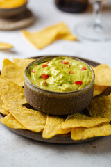 Nachos chips in a bowl with sauces guacamole and beer over white stone background.