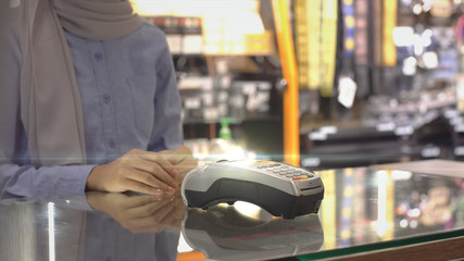 An upwardly mobile Asian Muslim man using a mobile phone - smartwatch to pay for a product at a sale terminal with nfc identification payment for verification and authentication