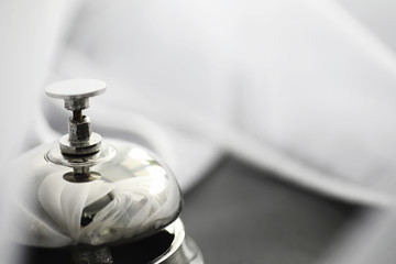 A shiny silver metal bell at the hotel reception. A table in the hotel at the concierge with a bell...