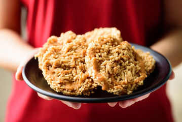 Sweet crispy rice with cane sugar drizzle on black plate holding by hand, Local Thai snack (Khao Tan)