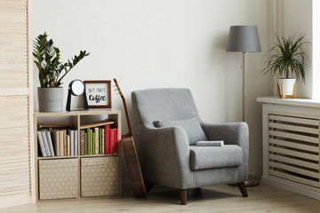 Background image of cozy reading nook in modern minimal interior, focus on grey armchair against white wall, copy space