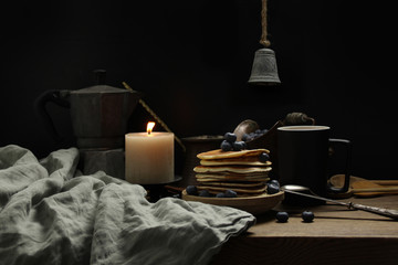 national dish pancakes, pancakes, pita with blueberries, linen napkin, poured with honey, candle burns, a cup of tea, an old mocha coffee machine, a concept of traditional cuisine