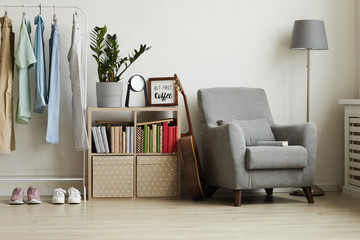 Full length view at studio apartment interior with minimal design, focus on comfy grey armchair and clothes rack against white wall, copy space