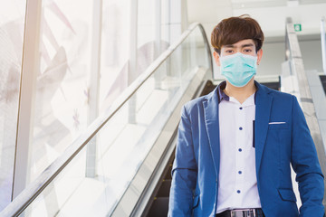 Fototapeta na wymiar The business man wearing protection face mask against coronavirus, PM 2.5 and cold while standing on escalator. Coronavirus and Air pollution pm 2.5 concept.