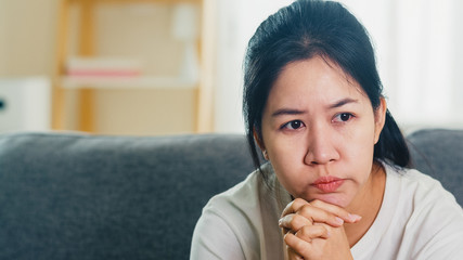 Depressed crying Asian business woman stressed with headache sitting on sofa in living room at house when social distancing stay at home and self quarantine time, coronavirus concept.