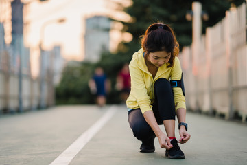 Beautiful young Asia athlete lady exercises tying laces for work out in urban environment. Japanese teen girl wearing sport clothes on walkway bridge in early morning. Lifestyle active sporty in city.