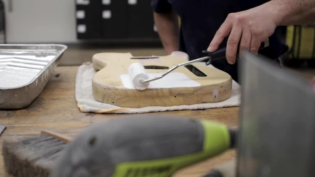 Man painting primer on a guitar body that he is refinishing