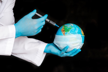 Globe earth in a medical mask and a syringe in the hands of the doctor close-up on a black background . The concept of the pandemic and the Coronavirus epidemic covid-19