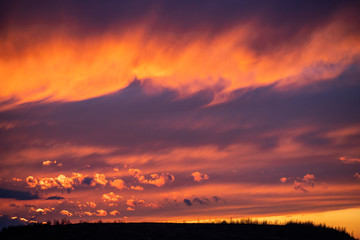 Bright red sunset among blue clouds. Mystical silhouettes in clouds