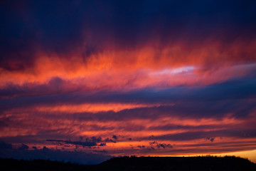 Bright red sunset among blue clouds. Mystical silhouettes in clouds