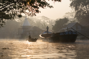 Boats transporting materials during sunrise in river channel near swamps in Barisal