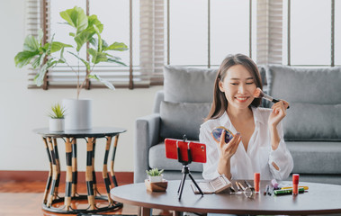 Happy beautiful Asian blogger woman recording video makeup cosmetic at home. Online influencer vlogger social media live steaming concept