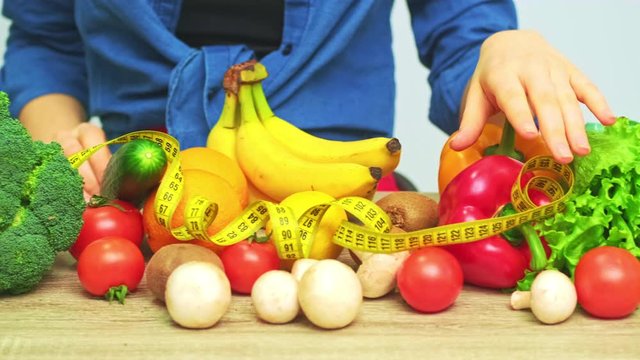 Young woman on a strict diet on the background of fresh vegetables and fruits