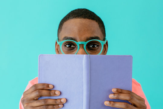 Portrait of a reader with glasses holding book and looking at camera, isolated on blue