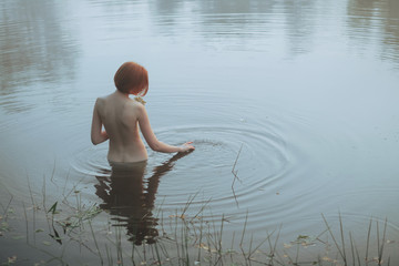Naked woman standing to waist in cold lake