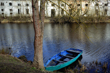 old boat on the river tied to a tree against the background of an abandoned building