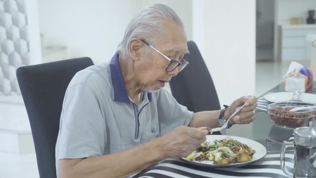 Elderly man eating fried rice and sitting alone in the dining table at home. Shot in 4k resolution