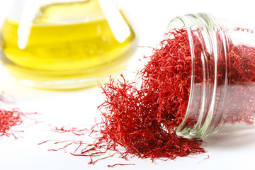 Dried saffron threads in a glass bottle and oil extract on a white background.