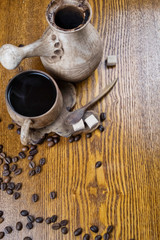 Ceramic coffee set in folk style close up. Juniper cup holder and coffee spoon. Fragrant coffee beans and brown sugar cubes. Coffee beans are scattered on a wooden table. Composition in warm colors.