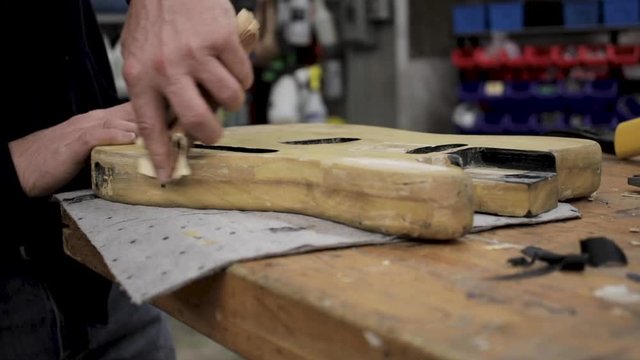 Man sanding the body of a telecaster guitar that he is refinishing.