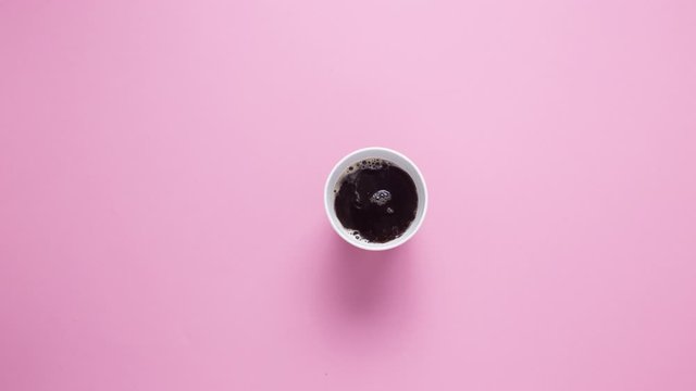 Stop motion. Paper cup with coffee on a pink background. Coffee is poured and a man's hand picks up a glass.