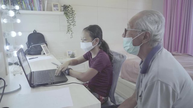 Little girl doing study from home with her grandfather while using a computer laptop on the bedroom during quarantine. Shot in 4k resolution