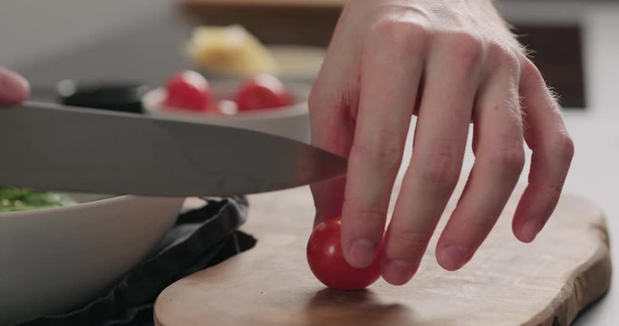 Slow motion closeup man cut cherry tomatoes in halves on olive board