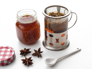Taza con infusión caliente, anís estrellado y un tarro con miel abierto sobre fondo blanco