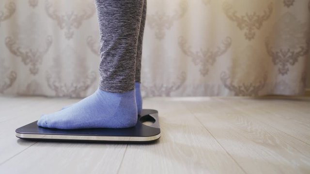 Woman in socks and leggings checks weight on electronic weight using display