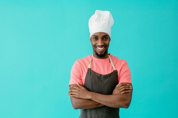 Portrait of a smiling young male chef with arms crossed, against blue studio background