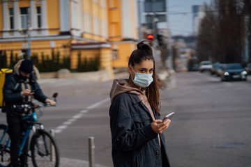 Girl in protective mask using smartphone outdoors. COVID 19. World coronavirus pandemic.