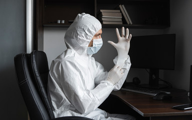 Man in protective suit and medical mask is wears rubber gloves at his working place at home during quarantine. Designer, artist, architect, businessman at remote work in a pandemic covid.