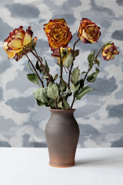 Bouquet of withered multicolor roses in brown ceramic vase. Grey wall background.