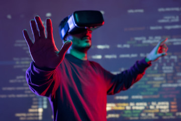 Young man gesturing hands while analyzing programming code in virtual reality goggles
