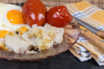 Barley porridge with fried eggs and canned tomatoes close-up
