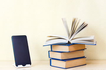 Stacks of old paper books back in the foreground modern digital gadgets mobile phone.