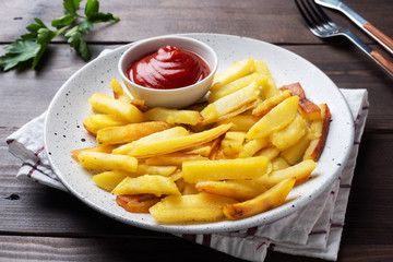 Fried French fries potatoes with tomato ketchup sauce on a plate. Wooden background. Copy space.