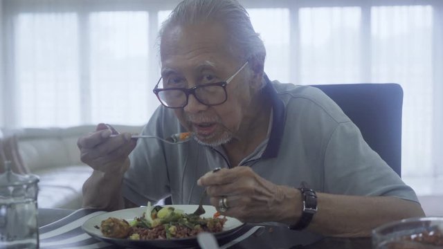 Lonely old man eating lunch while sitting in dining room at home. Shot in 4k resolution