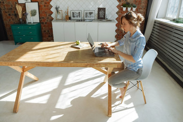 Woman using laptop working at home during quarantine and self-isolation. Fashionable kitchen....