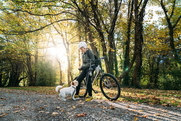 19/4/2020 Asian woman with a bike feeding a dog in autumn at the Botanic garden, Oamaru, New Zealand. Concept about exercise while social isolation from Coronavirus or Covid 19.
