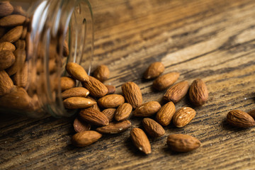 Almonds scattered on the wooden vintage table from a jar. Almond is a healthy vegetarian protein nutritious food. Almonds on rustic old wood.