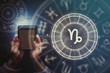 Female hands are holding a phone and an astrological circle with the zodiac sign Capricorn on a...