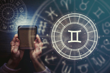 Female hands are holding a phone and an astrological circle with the zodiac sign Gemini against a...