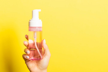 Close up of female hand holding cosmetics spray at yellow background with copy space