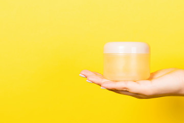 Female hand holding cosmetics jar at yellow background with empty space for your design