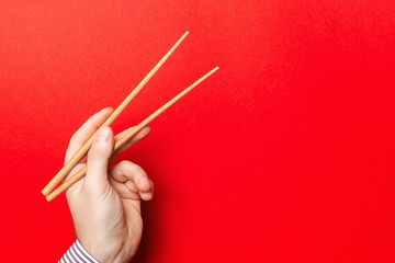 Male hand with chopsticks on red background. Traditional asian food with emty space for your design